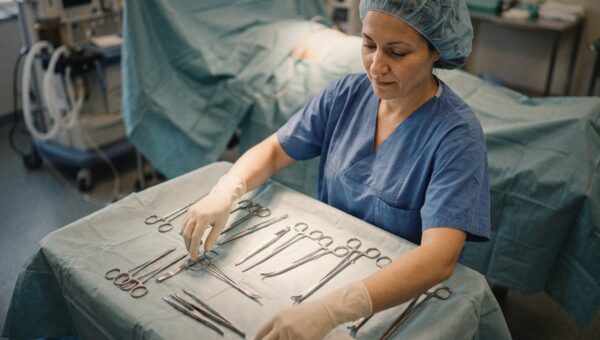 A scrub nurse arranging sterile surgical instruments on a tray, overhead light